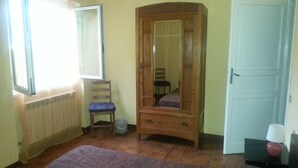 Un dormitorio con cama, armario de madera, una silla, ventana con cortinas y una puerta.
