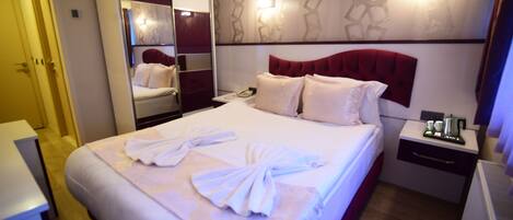 A hotel room with a neatly made bed, a bedside table with a phone and a coffee maker, and a mirror cabinet.