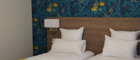 A double bed with a wooden headboard, two bedside tables, and a wall with a floral pattern.