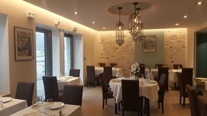 Un interior de restaurante con varias mesas y sillas, obras de arte enmarcadas en las paredes y una pared con textura de piedra.