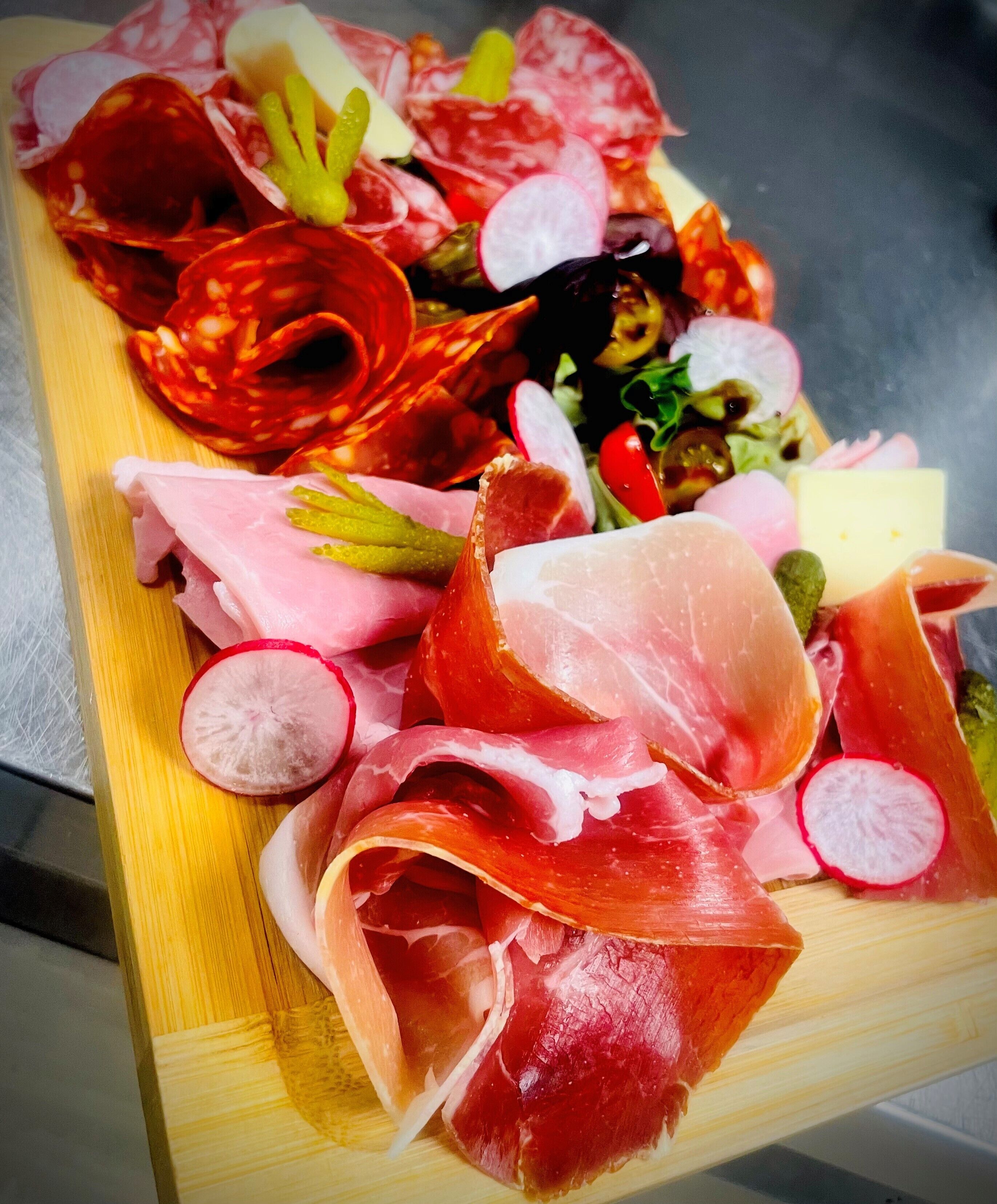 En träbricka med olika sorters lufttorkat kött, inklusive salami och prosciutto, samt skivade rädisor och körsbärstomater.