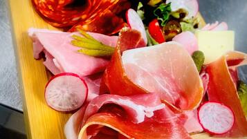 En träbricka med olika sorters lufttorkat kött, inklusive salami och prosciutto, samt skivade rädisor och körsbärstomater.