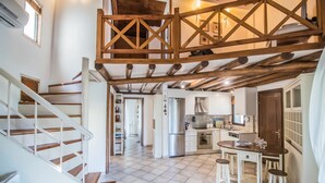 Eine geräumige Küche mit einer zentralen Kochinsel, Holzbalken an der Decke und einer Treppe zu einer weiteren Ebene.