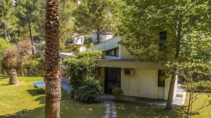 Ein modernes Haus mit überdachter Terrasse, umgeben von üppiger Vegetation und einem kleinen Teich.