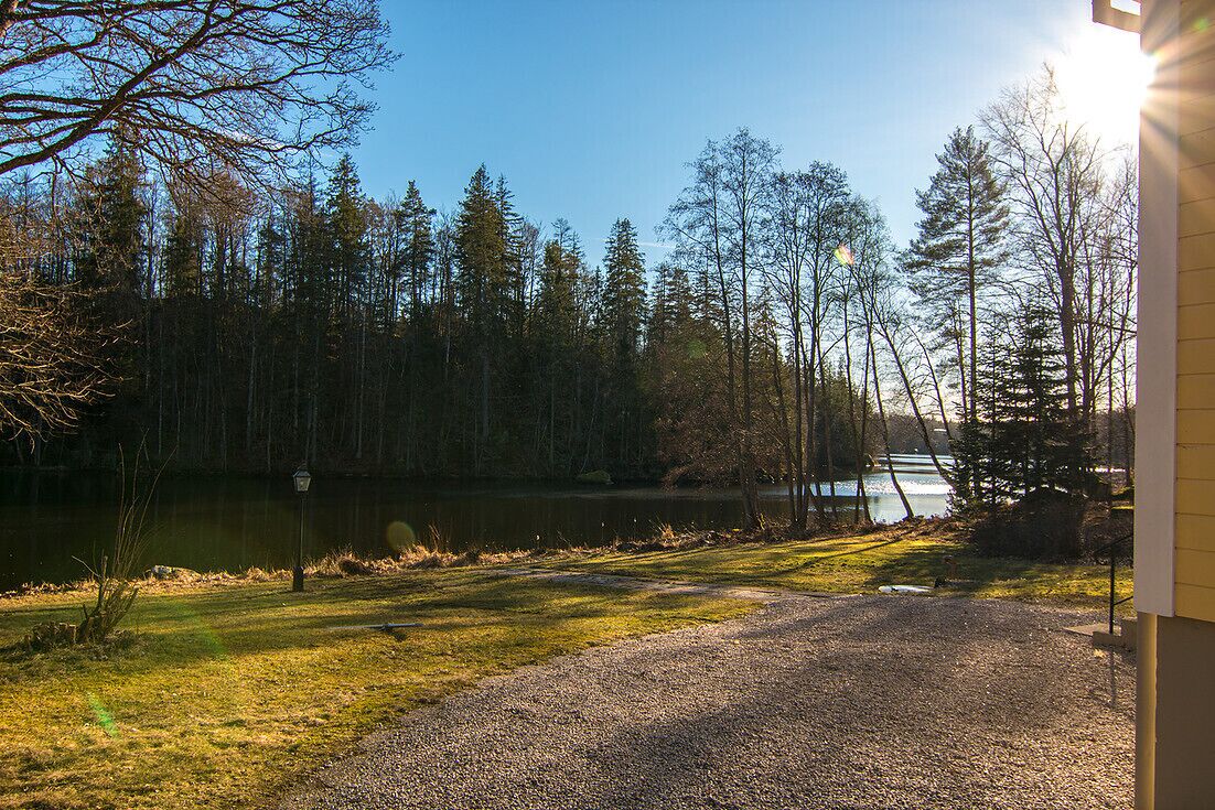 Ein Schotterweg führt zu einem Haus mit Seeblick und Blick auf den Wald.