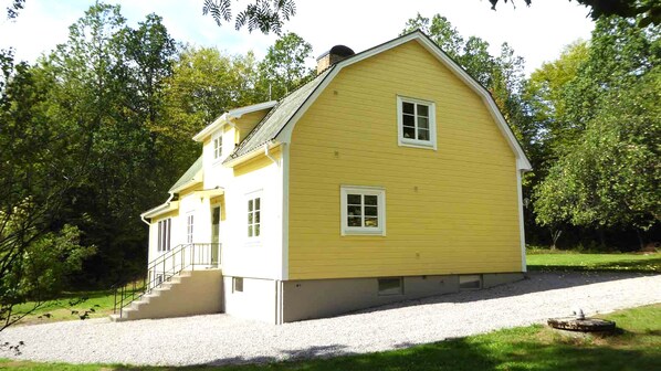 A two-story yellow house with a front porch and a staircase leading to the entrance. - Holiday Home Paradisvägen - 6 people (Ryd)