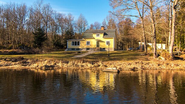 Ein gelbes Haus mit einer kleinen Veranda und einem Teich davor.