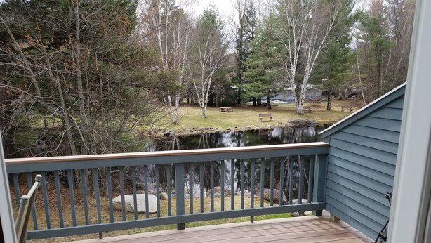 A wooden deck with a railing overlooking a pond and trees.