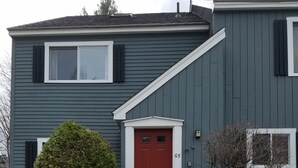 A two-story house with a red front door, a small porch, and a mailbox.