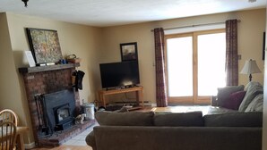 A living room with a brick fireplace, a television on a wooden stand, a sofa, and a dining area with a chair and table.