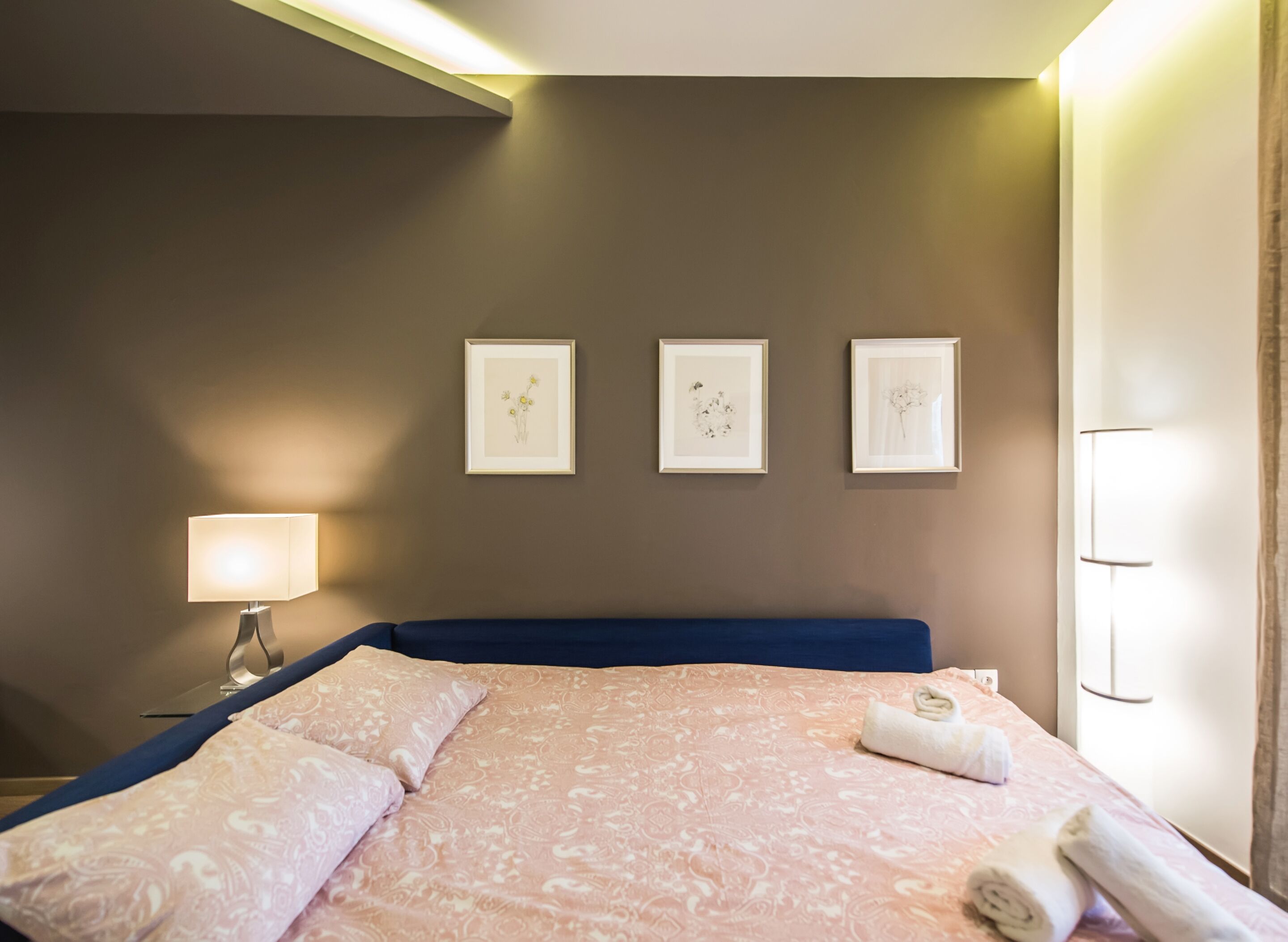 Une chambre d’hôtel avec un lit, une table de chevet, une lampe et trois tableaux encadrés accrochés au mur.