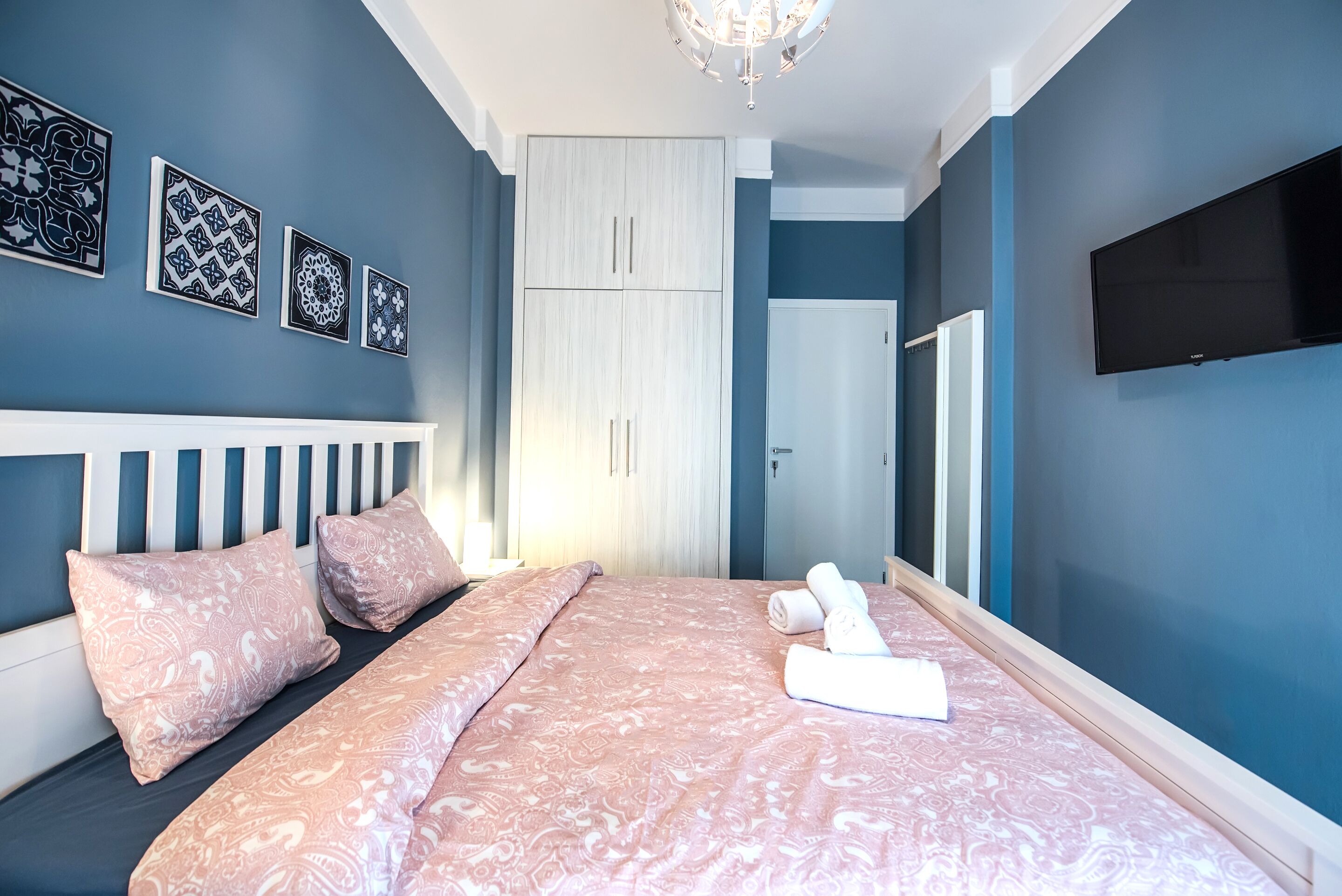 A bedroom with a bed, pillows, a TV, and artwork on the wall.
