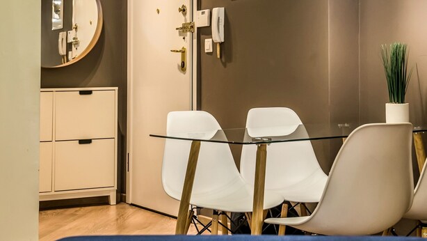 Een moderne kamer met een glazen tafel, witte stoelen, een ronde spiegel, een witte kast en een plafondlamp.