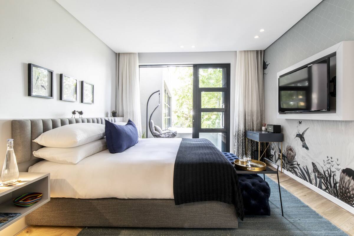 A modern bedroom with a large bed, a TV mounted on the wall, and a view of the outdoors.