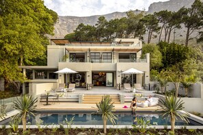Ein modernes, zweistöckiges Haus mit Swimmingpool, Sitzgelegenheit im Freien und Bergblick.