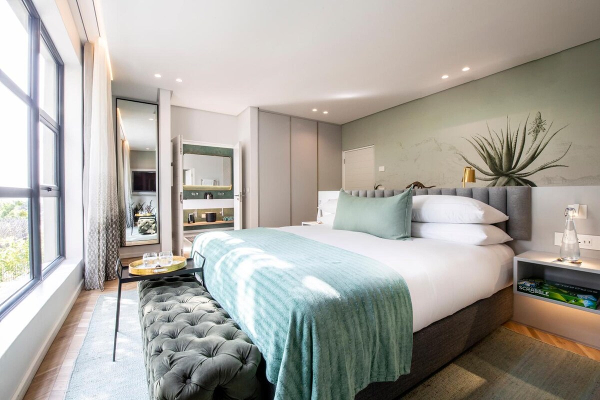 A modern bedroom with a large bed, bedside tables, a mirror, and a view of the outdoors.