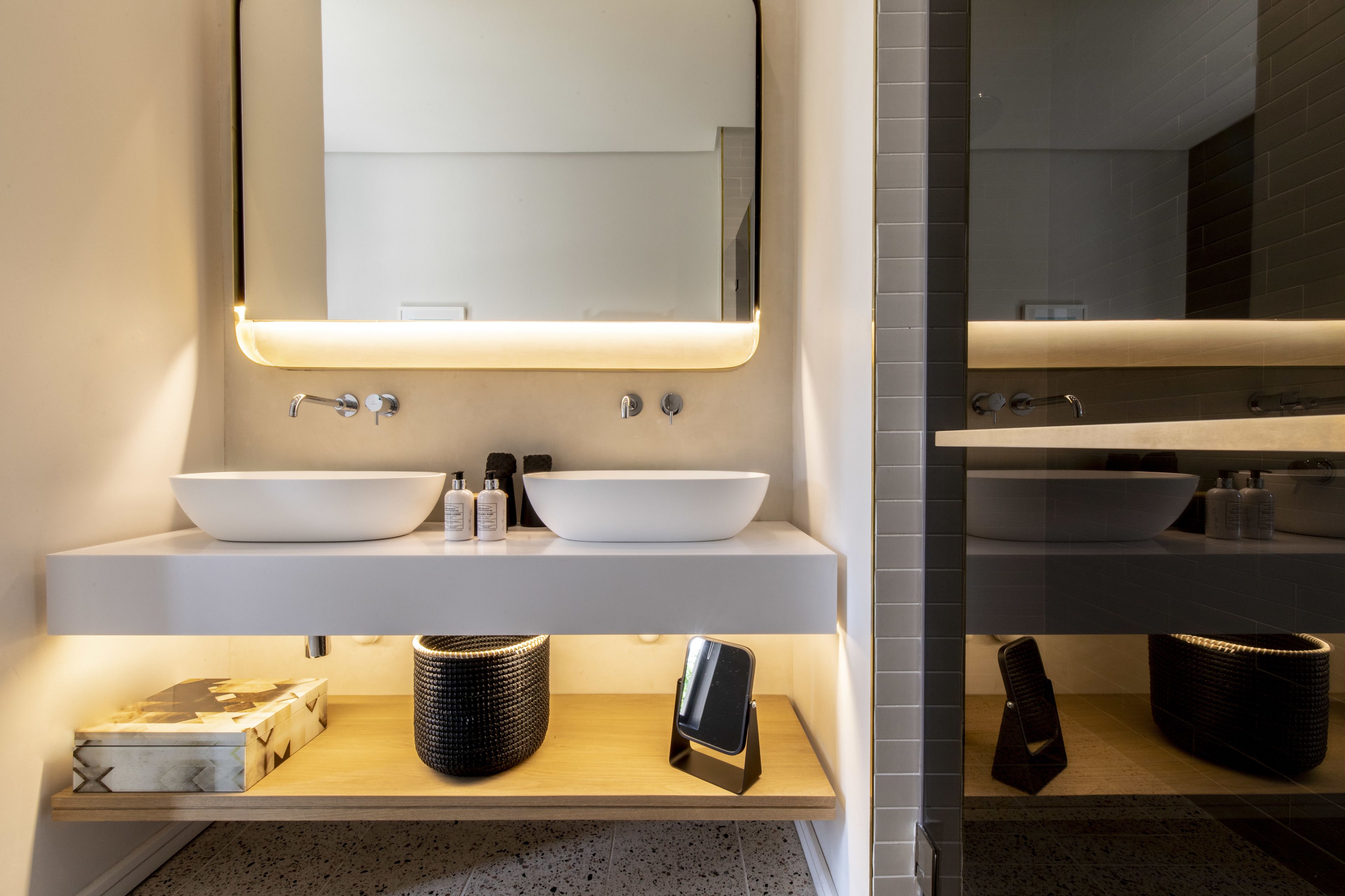 Un baño moderno con dos lavamanos, un espejo grande y una estación de carga para teléfono inteligente sobre una repisa de madera.