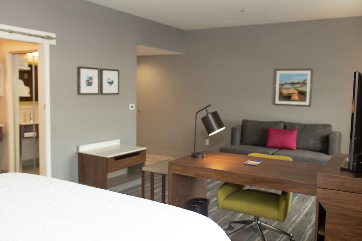 A modern hotel room with a bed, a desk, a chair, a sofa, and a TV.