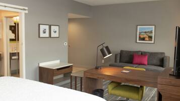A modern hotel room with a bed, a desk, a chair, a sofa, and a TV.