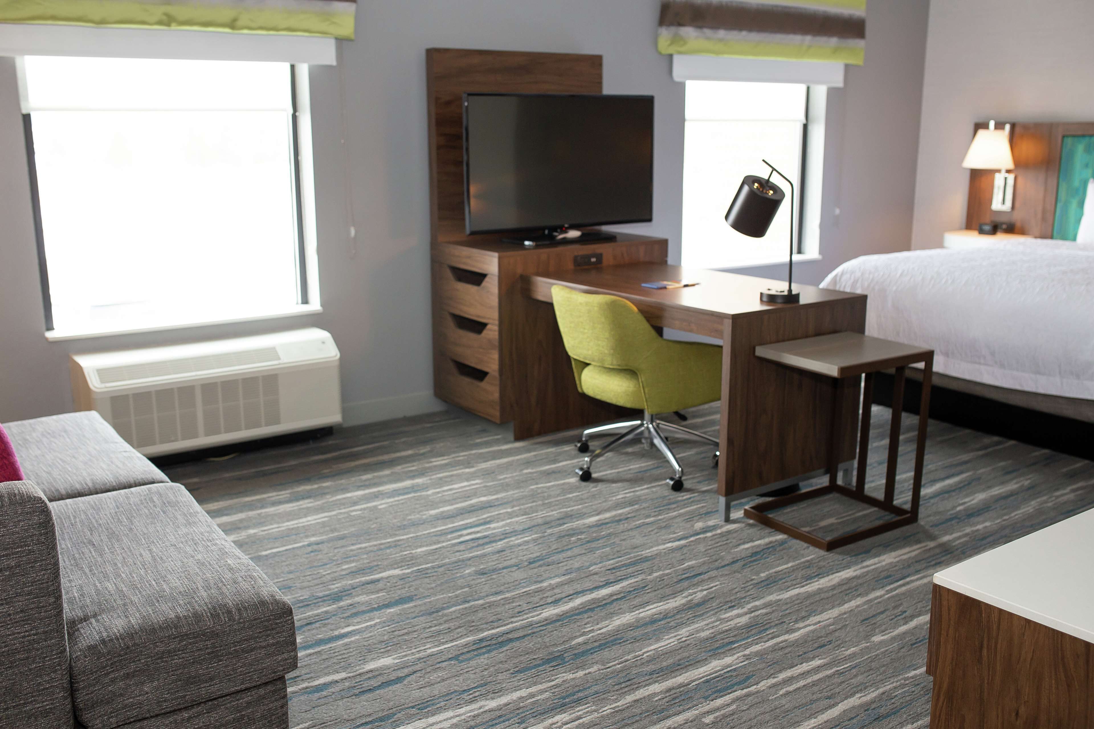 A hotel room with a bed, a desk with a chair, a television, and a window.