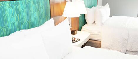 Habitación de hotel con cama, ropa de cama blanca, mesita de noche con lámpara y cabecero estampado.