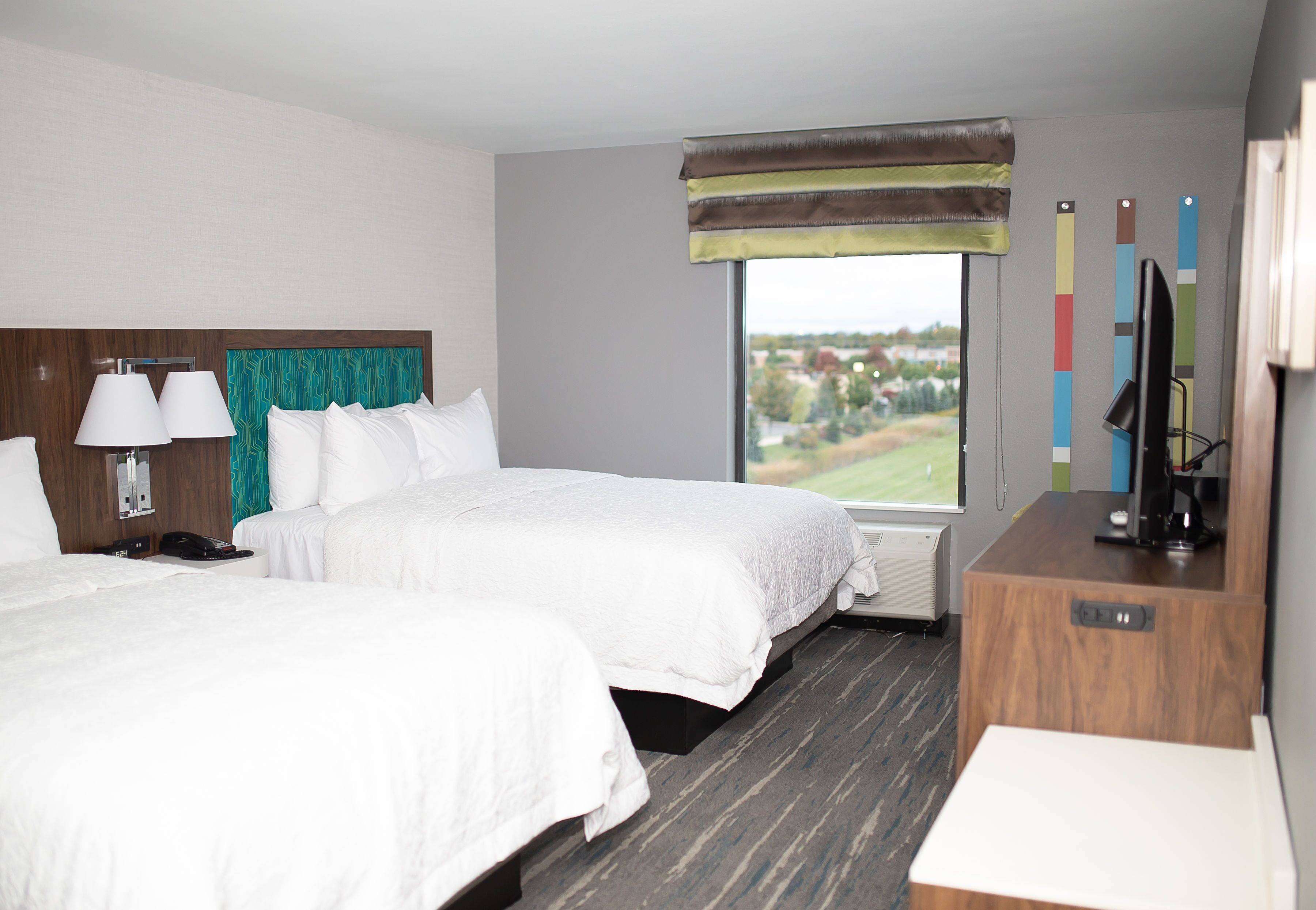 Une chambre d’hôtel avec deux lits, un bureau avec un ordinateur, un téléphone et une fenêtre donnant sur l’extérieur.