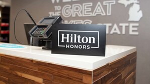 A reception desk with a 'Hilton Honors' sign, a phone, and a 'Welcome to the Great Lakes State' sign in the background. - Hampton Inn & Suites Dundee (Dundee)