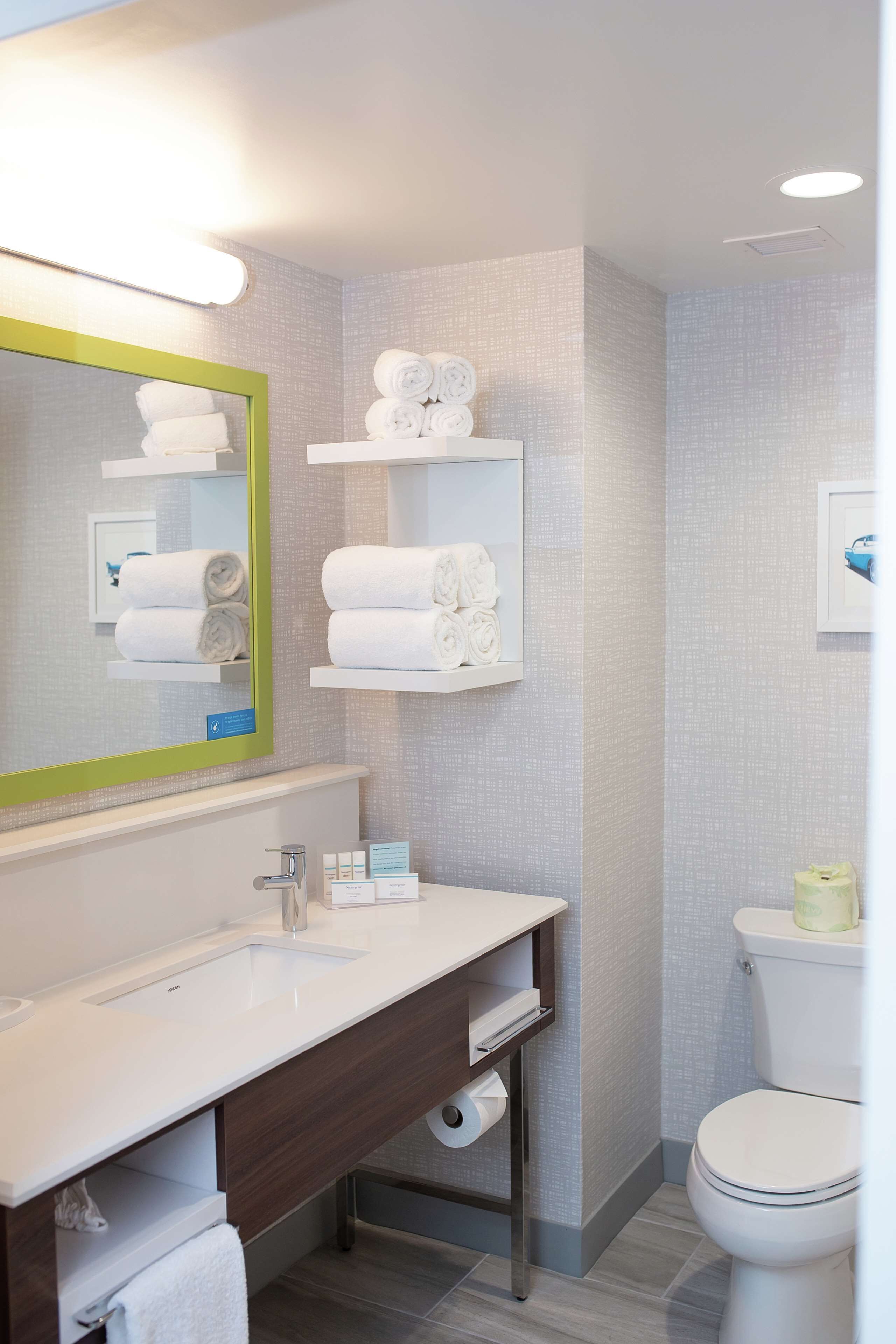 Een moderne badkamer met een wit wastafelmeubel, spiegel en toilet. Handdoekrekken met netjes opgerolde handdoeken.