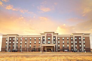 Un hotel Hampton Inn & Suites con fachada de ladrillo, múltiples ventanas y cielo despejado.