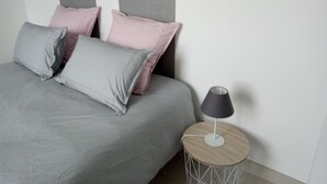 Una cama con almohadas grises y rosadas, una mesita de noche redonda con una lámpara y un cabecero gris.