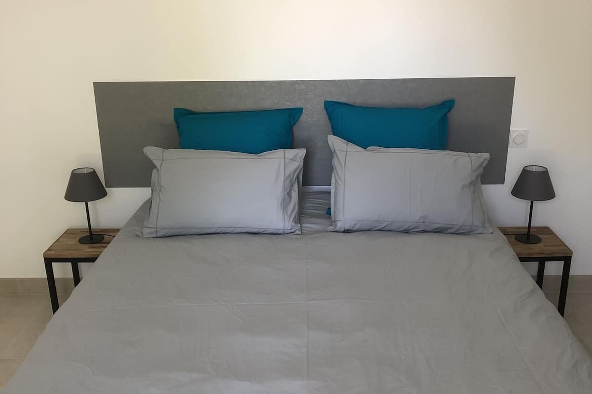 A bed with a grey headboard, two blue pillows, and two grey pillows. There are two nightstands with lamps on either side of the bed.