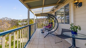 Un balcon abrité avec un fauteuil suspendu, une table et un pot de fleurs.