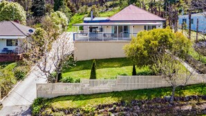 Une maison avec un toit rouge, un balcon et un jardin entouré d’une clôture en bois.