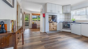Une cuisine moderne avec des meubles blancs, un four encastré et une fenêtre équipée de stores.