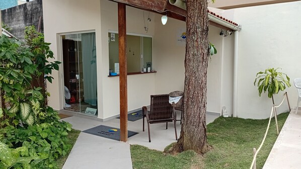 Un área de estar al aire libre techada, con una silla de mimbre, un árbol y una planta en maceta.