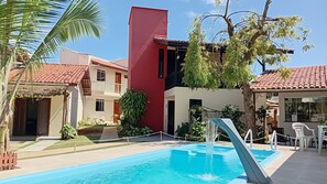 A swimming pool with a water feature, surrounded by buildings with red-tiled roofs and a mix of architectural styles. - Solaris do Atlantico (Ilhéus)