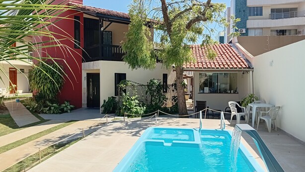 Una piscina con solárium empinado, un edificio rojo y un edificio blanco con balcón.