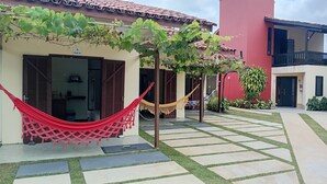 Un patio con una hamaca, una puerta con la leyenda 'FLAT 01', y un edificio rojo.