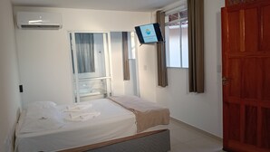 Un dormitorio con cama, televisor montado en la pared, ventana con cortinas y puerta de madera.