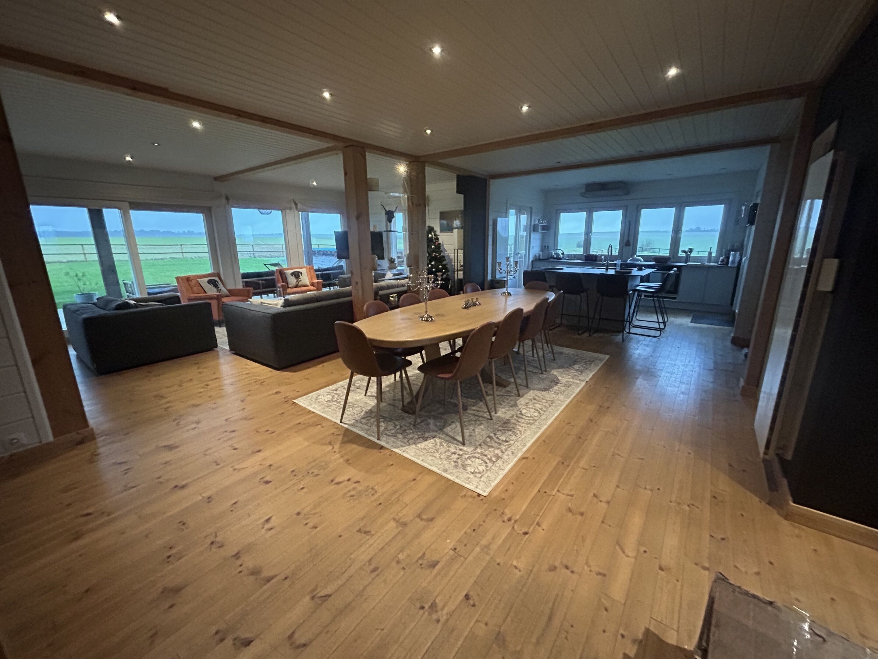 A spacious living area with a wooden floor, a dining table, and a kitchen in the background.