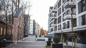 A modern urban street with multi-story buildings, a brick structure, and a gated entrance.