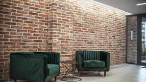 Een kamer met een bakstenen muur, twee groene fauteuils en een kleine tafel.