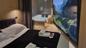Hotelkamer met een bed, een televisie waarop een berglandschap te zien is, een wellnessruimte met een jacuzzi en een douche.