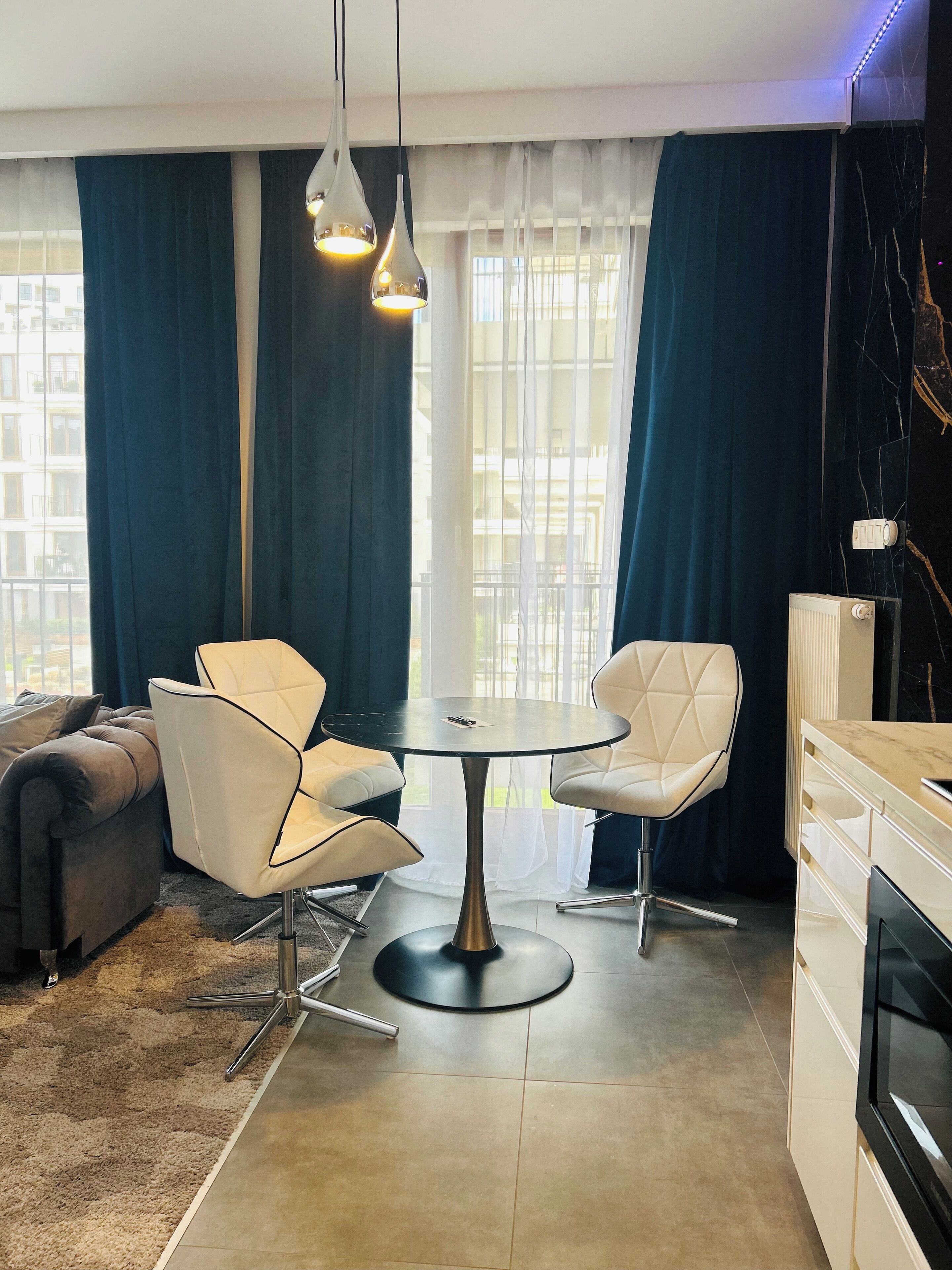 A modern living room with a round table, two white chairs, a sofa, and a kitchen area with a stove.