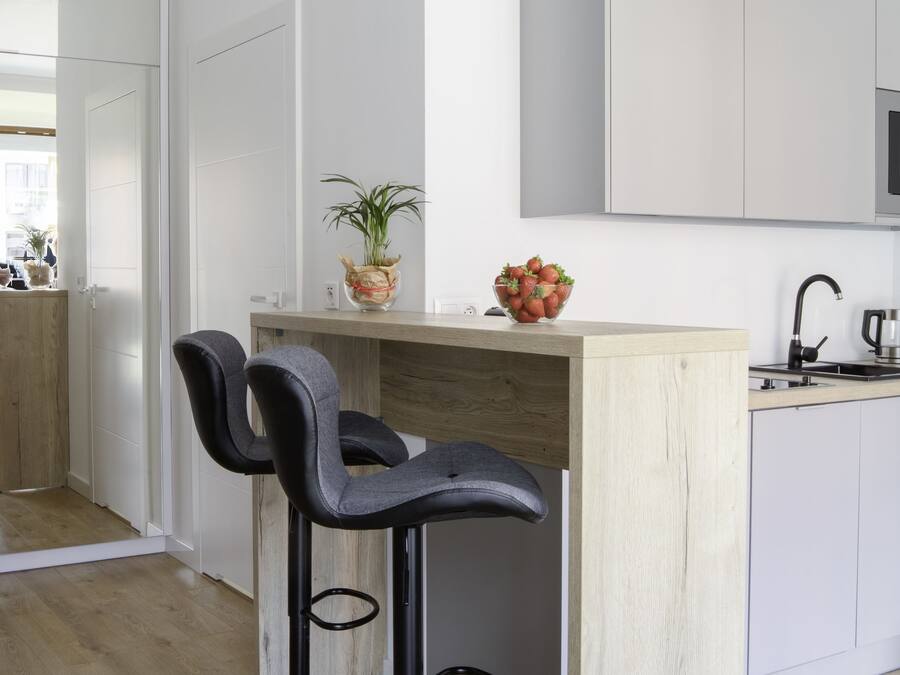 Una cocina moderna con dos taburetes de bar, una isla de madera y una encimera blanca.