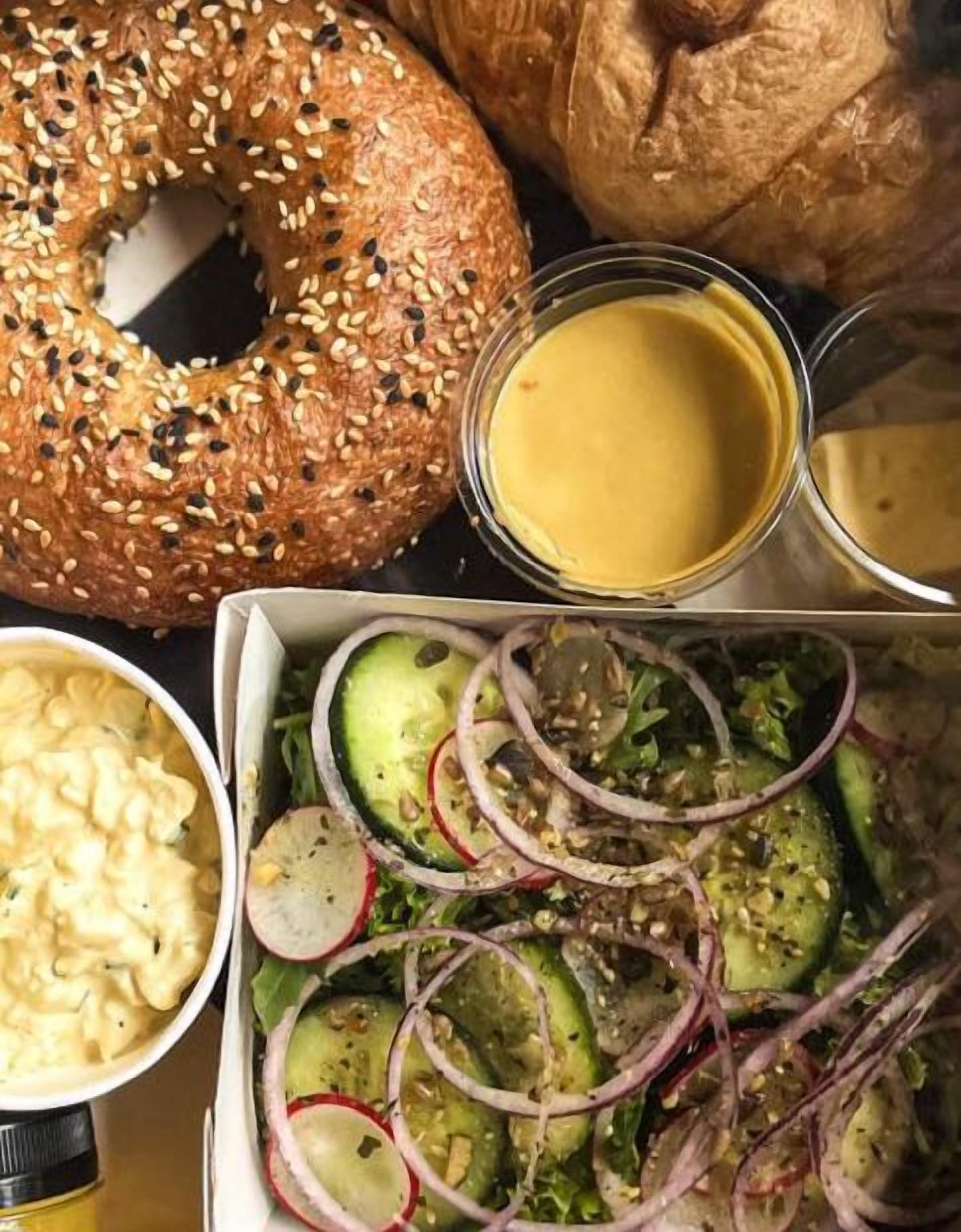 Una comida con bagel, ensalada, macarrones y una taza de sopa.