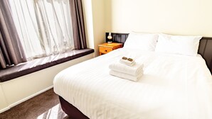 Quarto de hotel com cama, mesa de cabeceira, abajur e janela com cortinas.