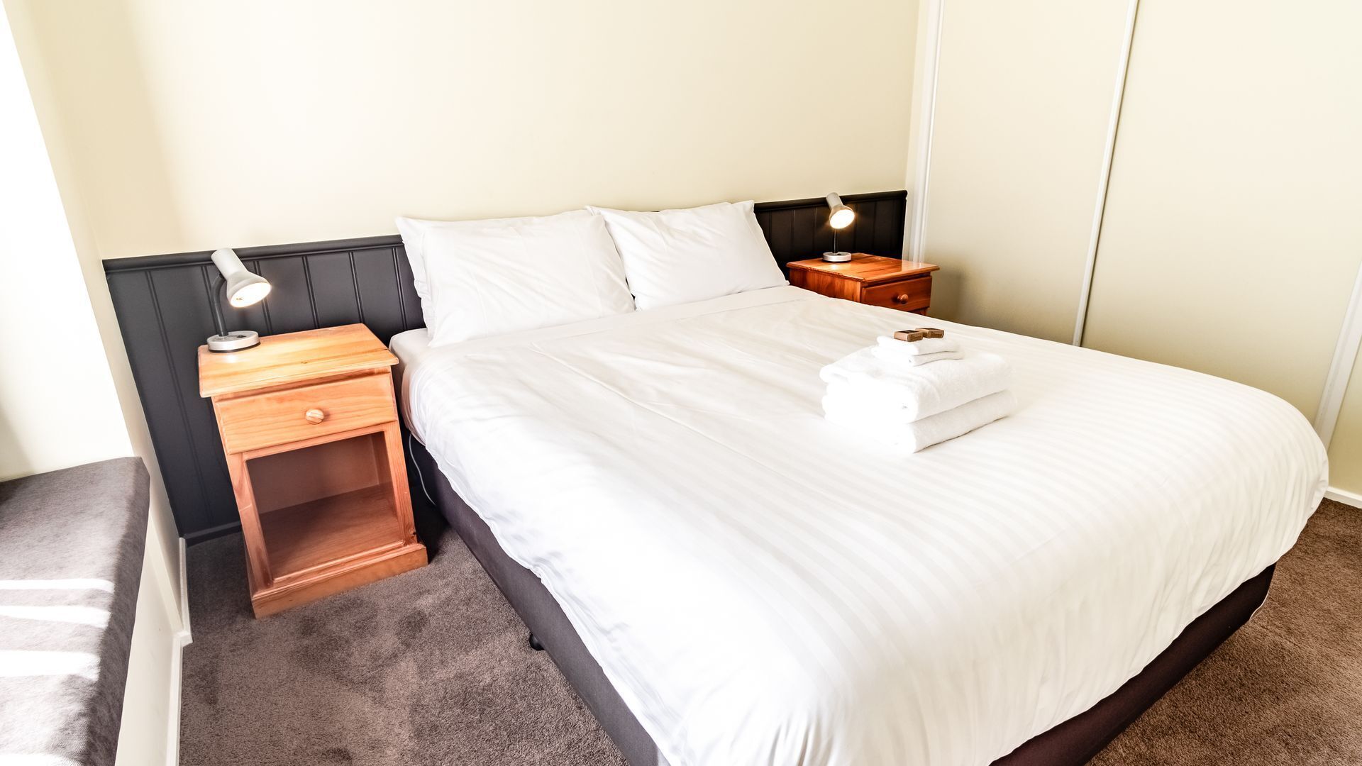 A neatly made bed with white linens, two bedside tables with lamps, and a wooden nightstand.