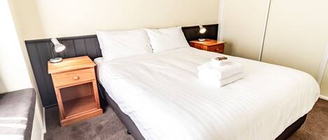 A neatly made bed with white linens, two bedside tables with lamps, and a wooden nightstand.