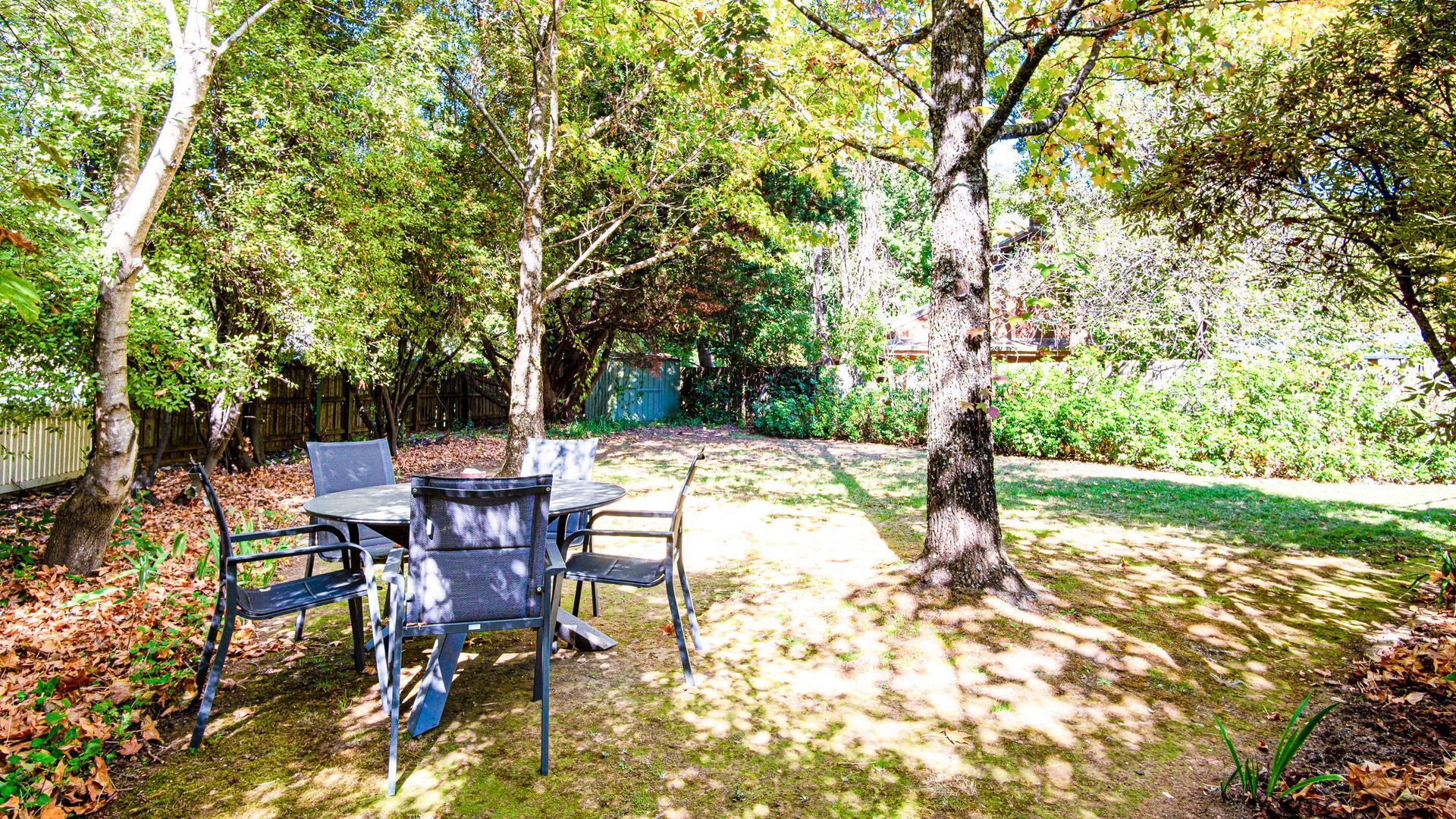 Une terrasse extérieure avec une table et des chaises, entourée d’arbres et d’une pelouse.